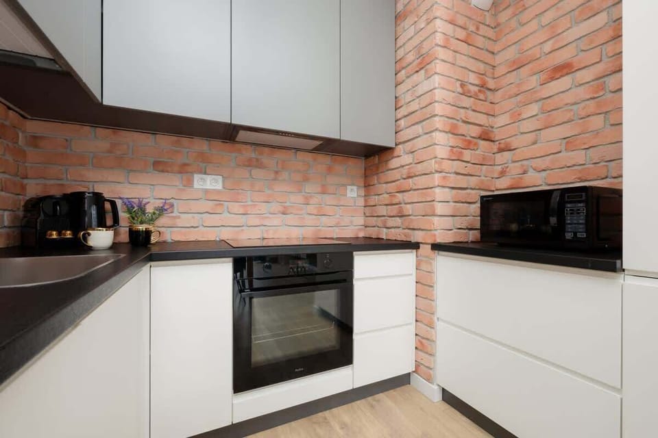 A close-up of a dishwasher built into a sleek kitchen with red brick backsplash and white cabinetry.