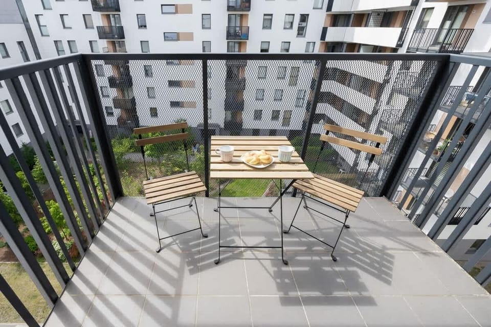 A balcony with black railings, garden furniture, and a view of nearby apartment blocks.