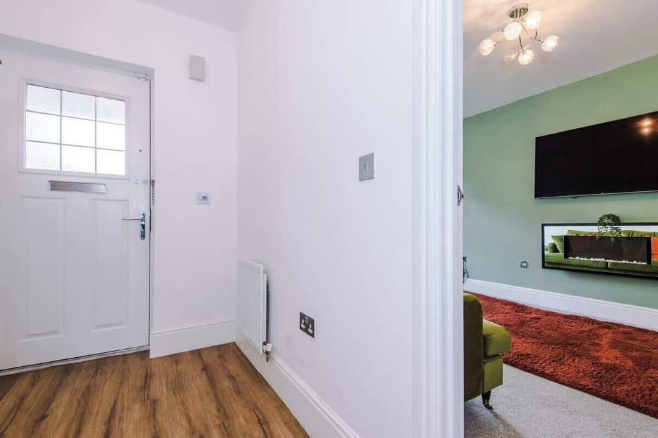 A bright, contemporary living space with plush green sofas, warm orange cushions, and a soft rug — designed for ultimate relaxation and cosy evenings.