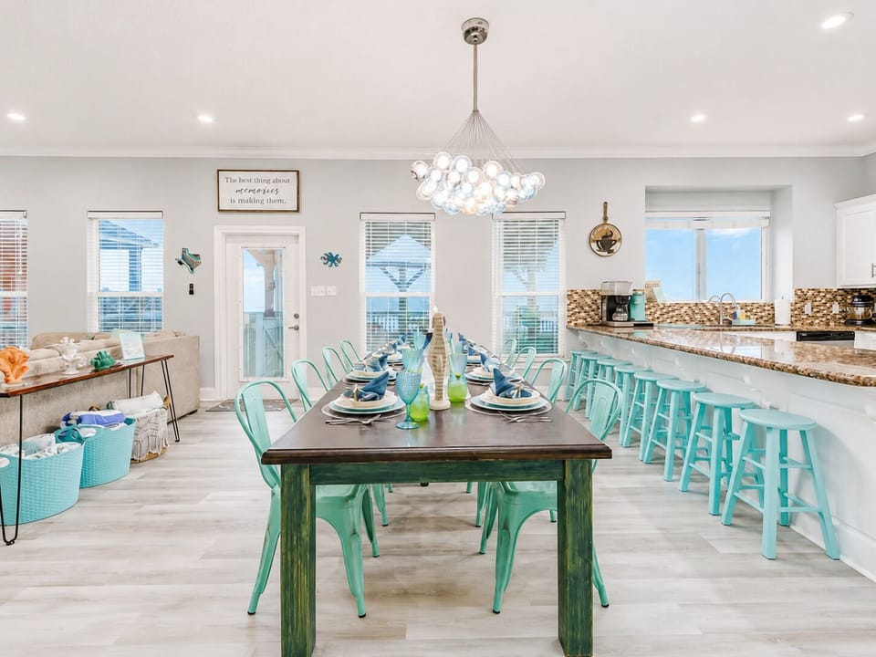 Open dining and kitchen area with a spacious table, breakfast bar seating and bright coastal finishes designed for easy group meals and entertaining.