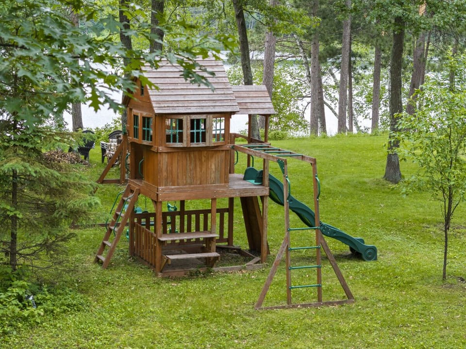 Private backyard playground equipment surrounded by tall green trees.