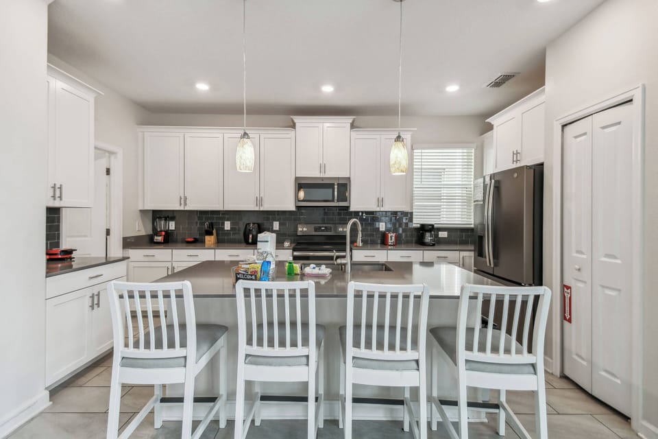 This bright kitchen features sleek white cabinetry, a spacious island with seating for four, and elegant gray countertops that enhance the stainless-steel appliances, creating an inviting space for your culinary adventures.