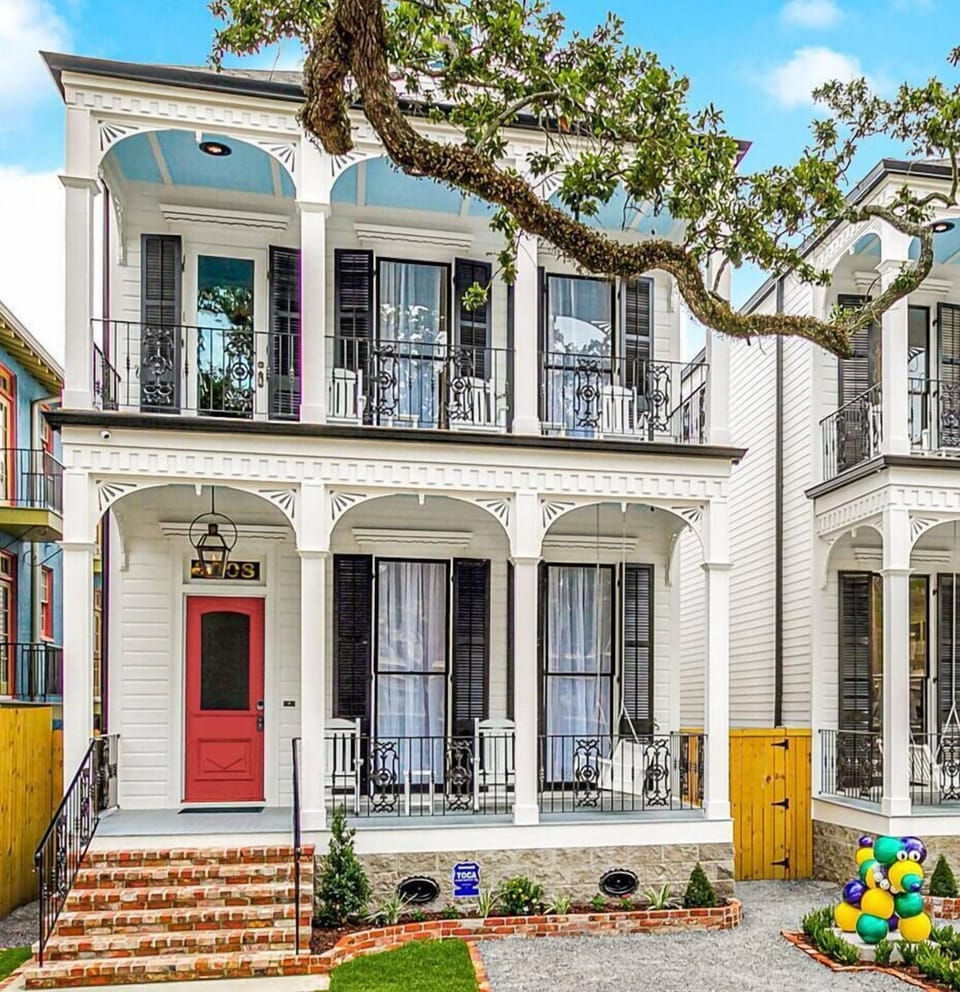 The front view of one of our two 5-bedroom, 5-bath homes on world-famous Canal Street, featuring the iconic "MARDI GRAS BEAD DOG" statue, offers a captivating scene with streetcars passing by.