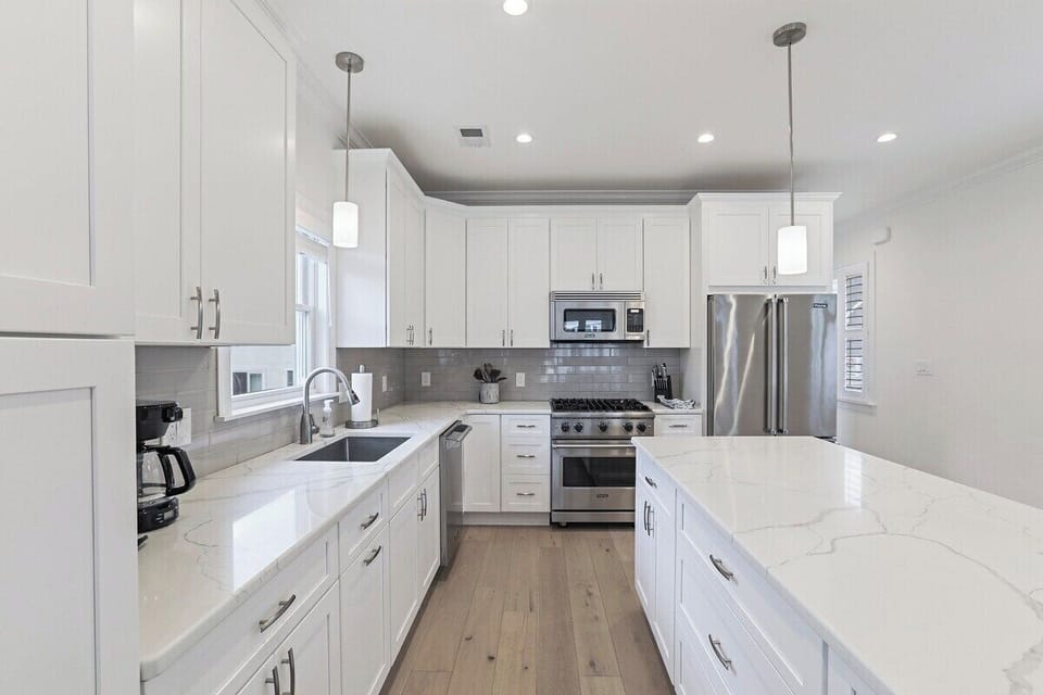 Whip up a meal in the fully equipped kitchen, featuring sleek white shaker cabinets, elegant quartz countertops, and modern stainless steel appliances. A spacious central island provides additional prep space and casual seating.