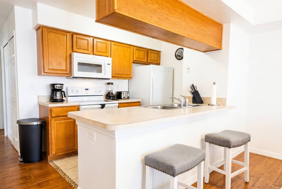 Step into a warm and functional kitchen featuring rich wooden cabinets and a spacious countertop that invites culinary creativity. The soft gray bar stools provide a cozy spot for casual meals, enhancing the welcoming atmosphere.