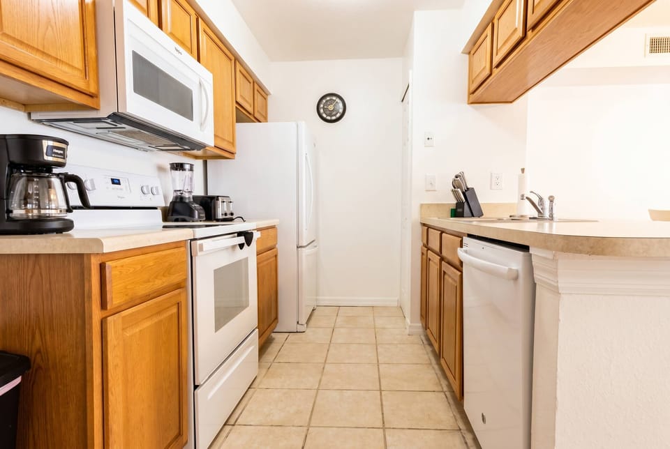This functional kitchen has warm wooden cabinetry and modern appliances, creating a welcoming space for meal preparation. The spacious layout and stylish tile flooring offer both comfort and ease while cooking.