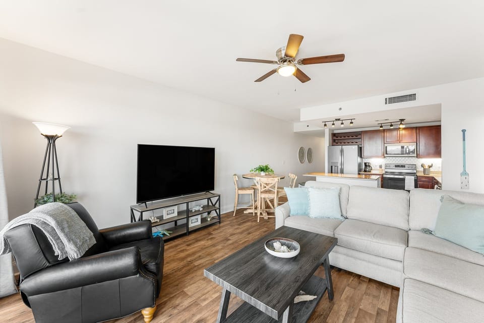 Modern living room with open kitchen and dining area featuring wood flooring and ceiling fan.