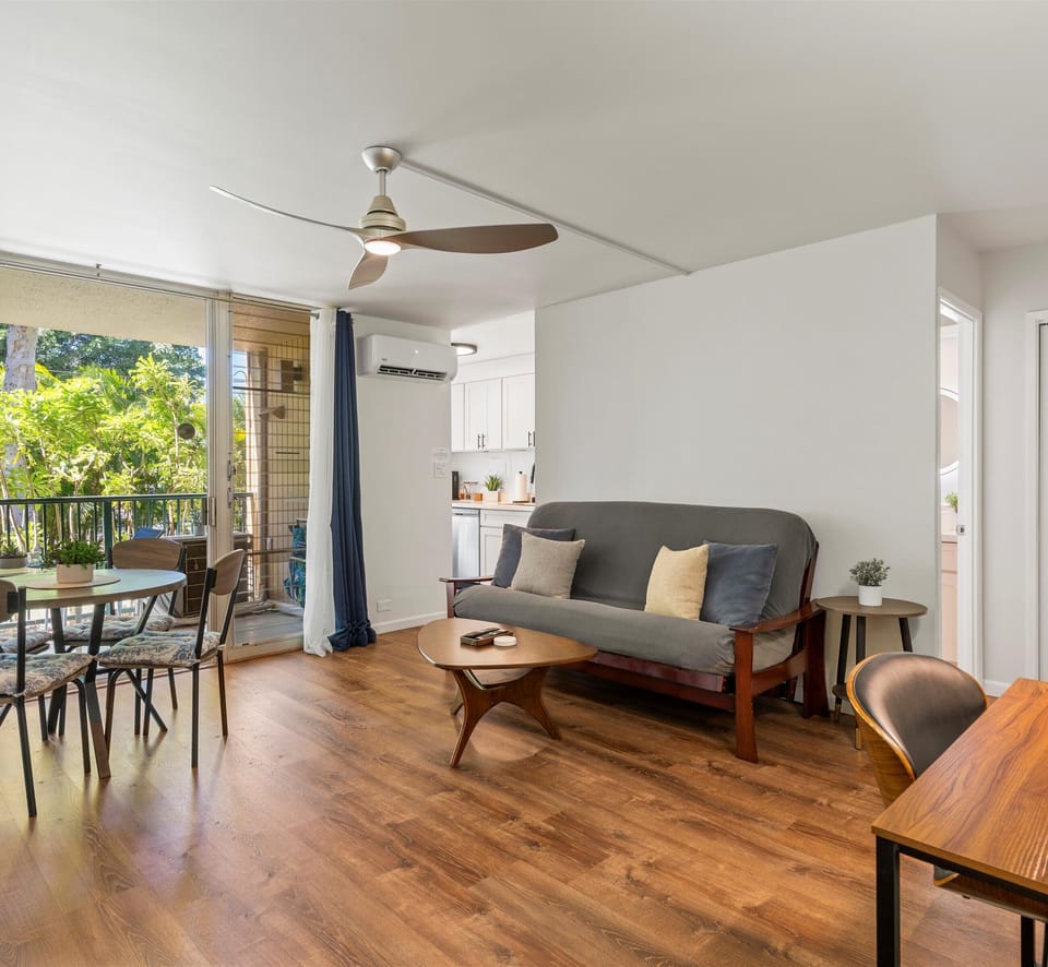 Your bright, open living room blends mid-century charm with modern comfort, featuring warm wood floors, a cozy sofa, and a breezy balcony overlooking lush greenery.