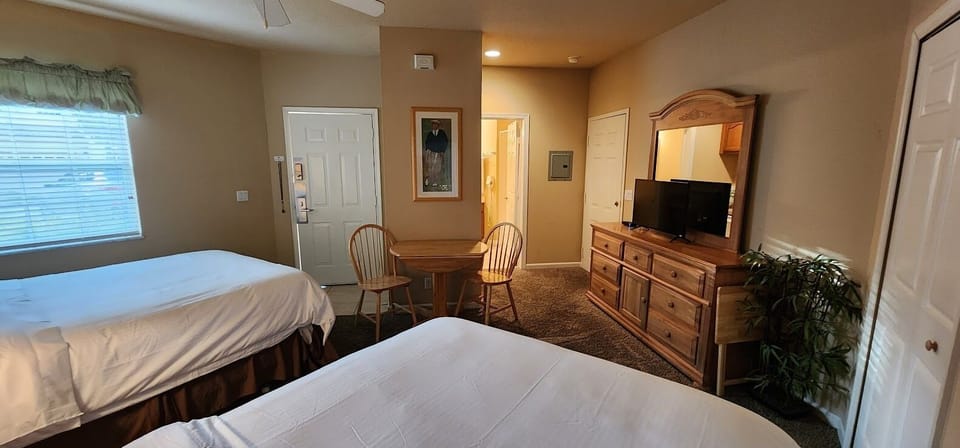 Spacious bedroom with two beds, dresser storage, TV, and a small table with seating.