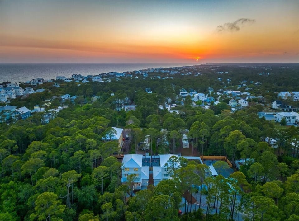Aerial view captures a stunning sunset over this coastal community nestled among lush trees near the beach.