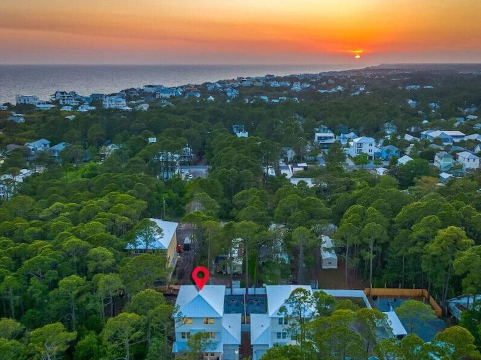 Coastal neighborhood bathed in golden sunset light, with tree-lined streets leading toward the ocean horizon.