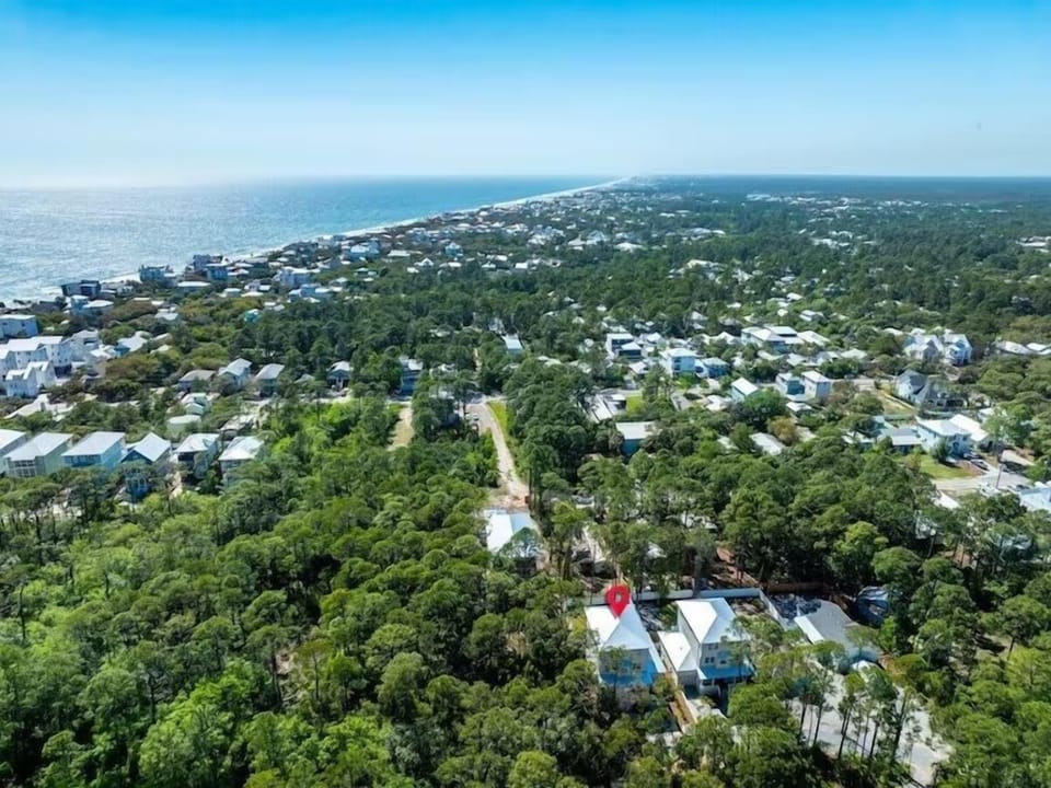 Aerial view of a coastal community with lush tree canopy, residential homes, and the beach just moments away from this charming neighborhood.