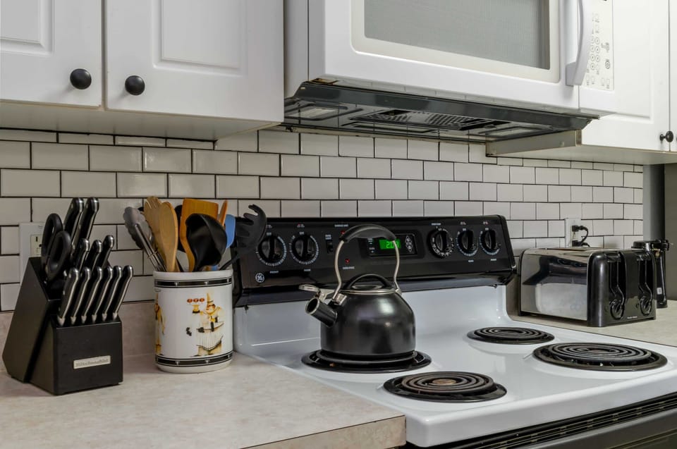 Functional kitchen area with electric stove, microwave, and essential cooking utensils.