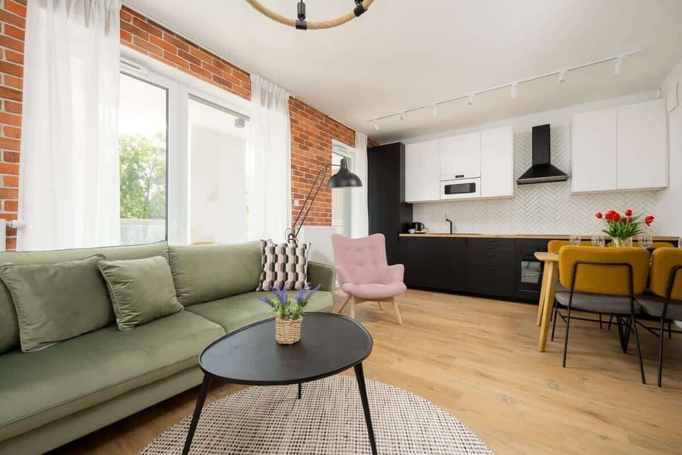 A cozy living room with green sofa, a circular coffee table, and a pink armchair, decorated with modern art and exposed brick walls, creating a stylish and warm ambiance.
