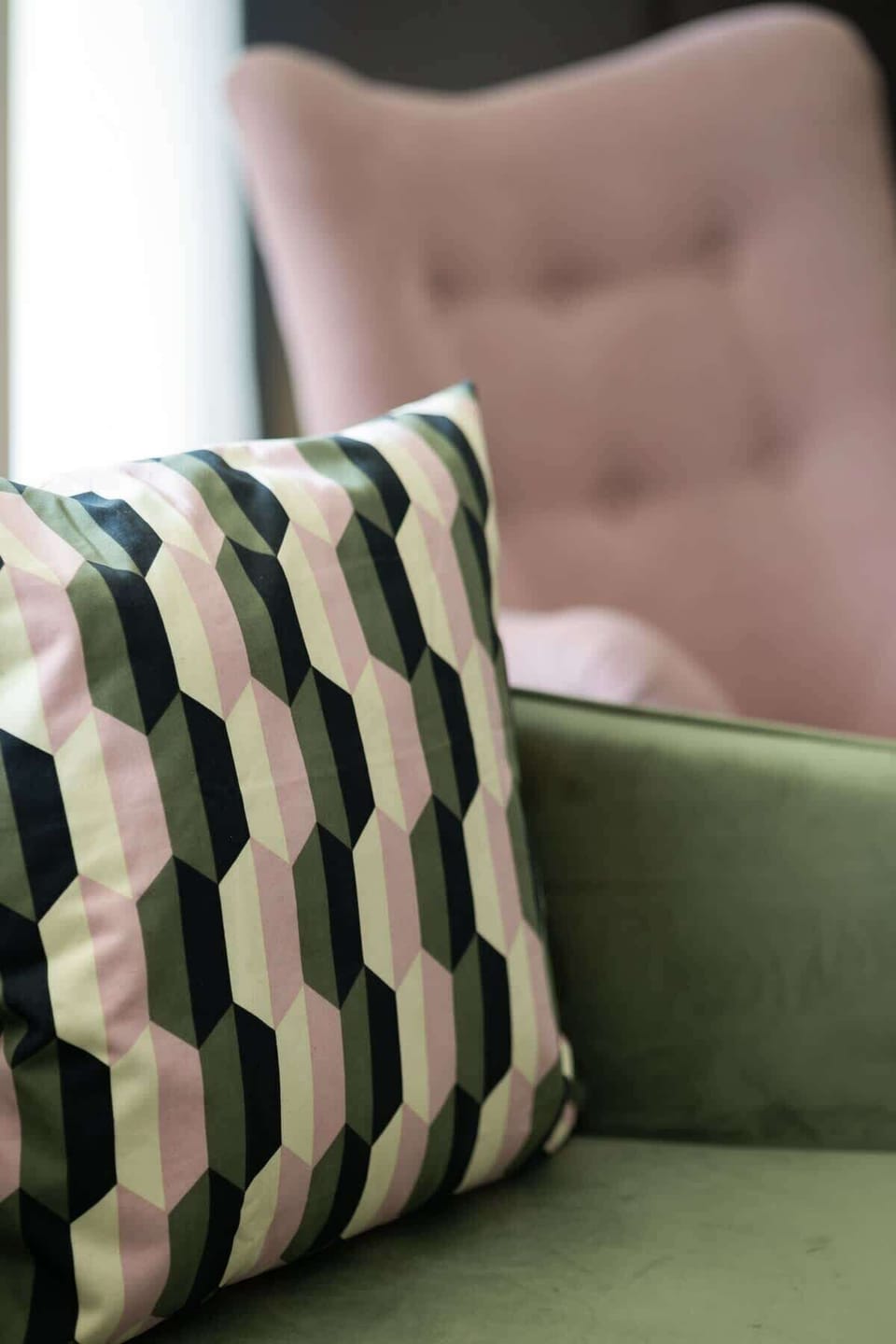 A stylish green cushion with a geometric, chevron-patterned pink and green pillow, adding a pop of color to a neutral backdrop.