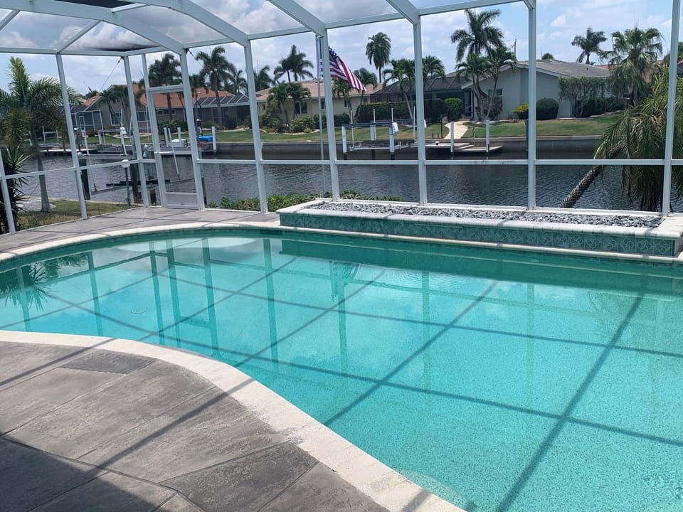 HEATED POOL W/WATERFALL, GREY COOL DECK, VIEW OF SALT WATER CANAL W/JUMPING FISH