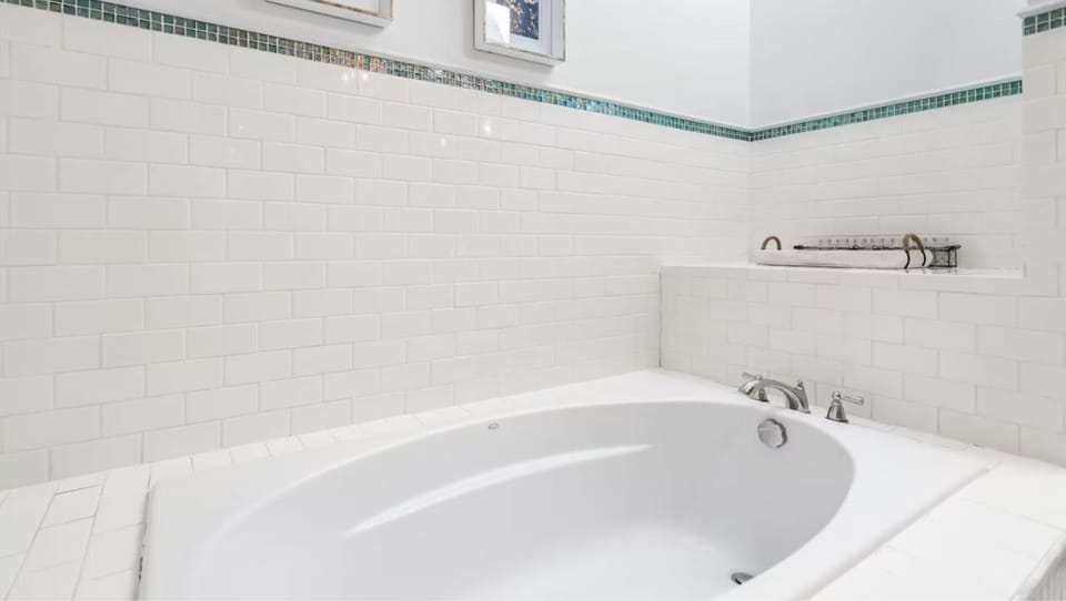 Sink into this pristine soaking tub surrounded by elegant white subway tiles and soothing green mosaic accents for your perfect relaxation retreat.