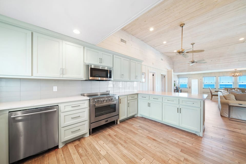 Your spacious kitchen features coastal-inspired seafoam cabinetry, gleaming countertops, and opens beautifully to ocean views beyond.