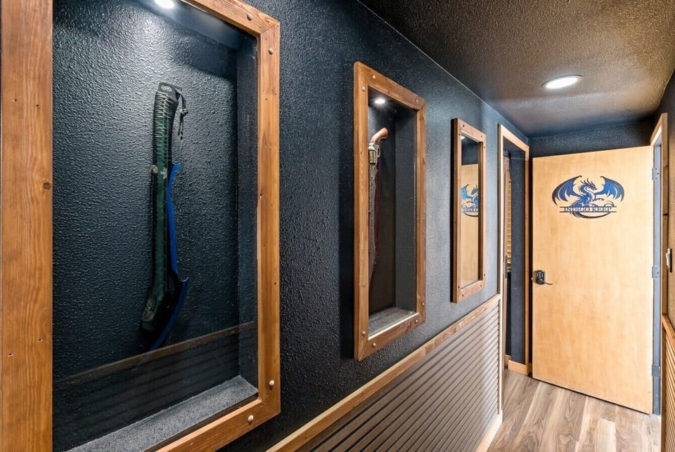 Built by hand and recessed into the wall, these wooden display cases showcase a fantasy scythe, a steampunk revolver/sword, and a skull dragon war axe. Each piece is individually lit, lining the corridor all the way to the entrance.