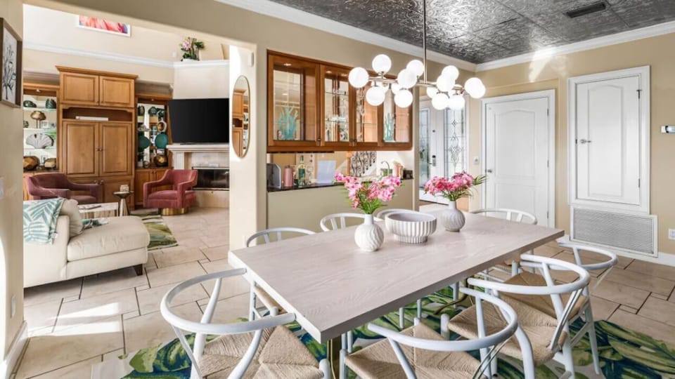 Gather around your bright dining table with modern lighting and fresh flowers, overlooking your comfortable living space with entertainment center.