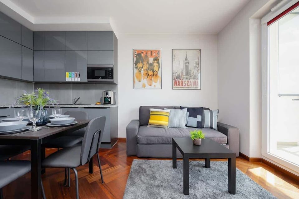 A cozy living room corner with a gray sofa, TV, and dining table. Ideal for unwinding after a long day.


