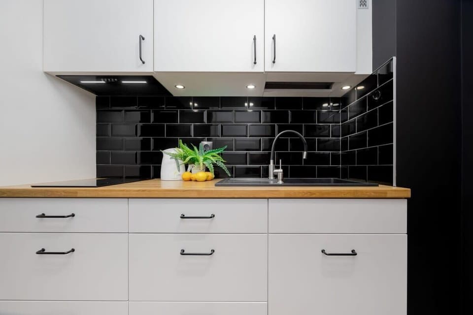 A modern kitchen featuring sleek white cabinets and a black tiled backsplash. A potted plant adds a touch of freshness to the countertop.