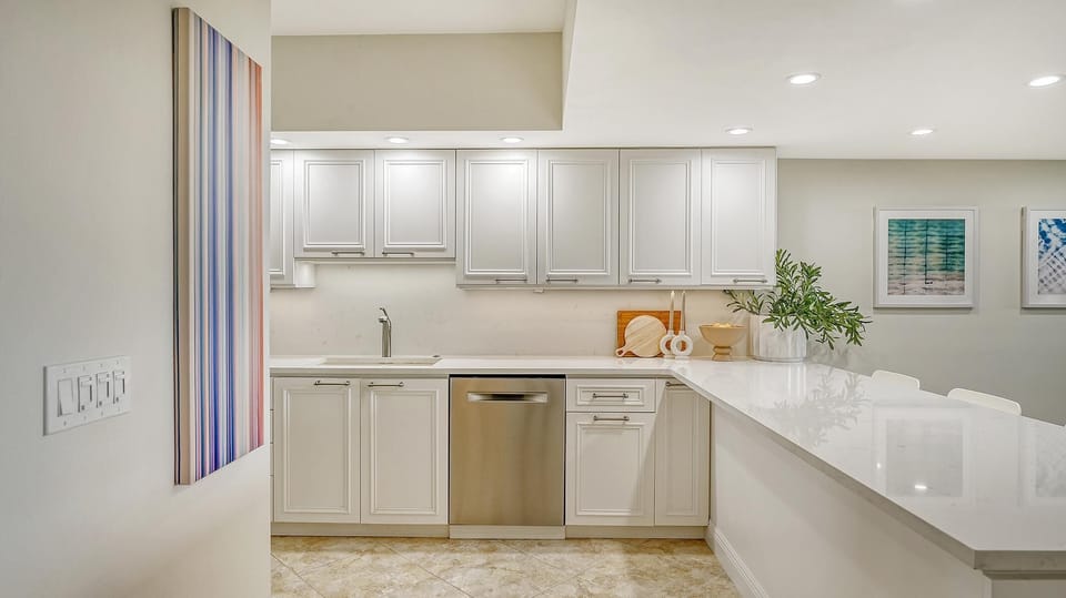 White cabinetry lines the kitchen with a stainless dishwasher, marble countertops, and recessed ceiling lights.