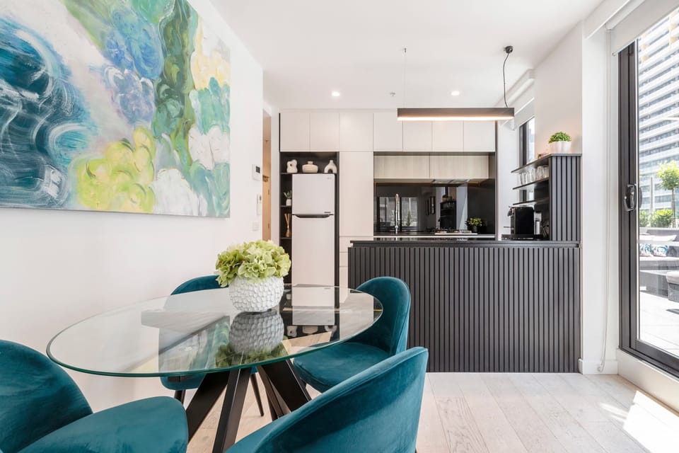 KITCHEN AND DINING AREA: Dining nook featuring a glass table and velvet chairs beneath vibrant artwork