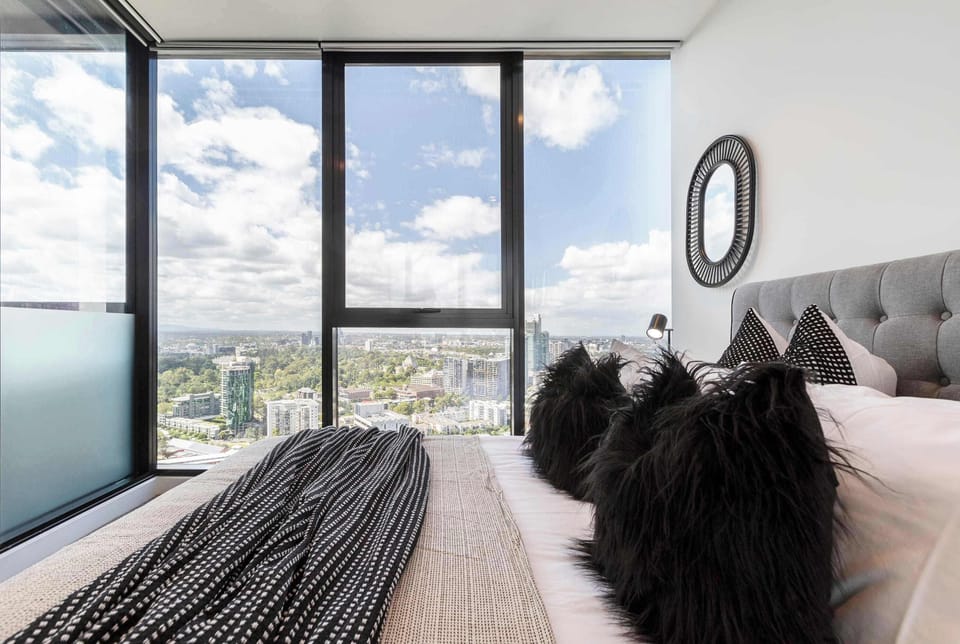 BEDROOM 2: Comfortable queen bed surrounded by stunning city views through floor-to-ceiling windows