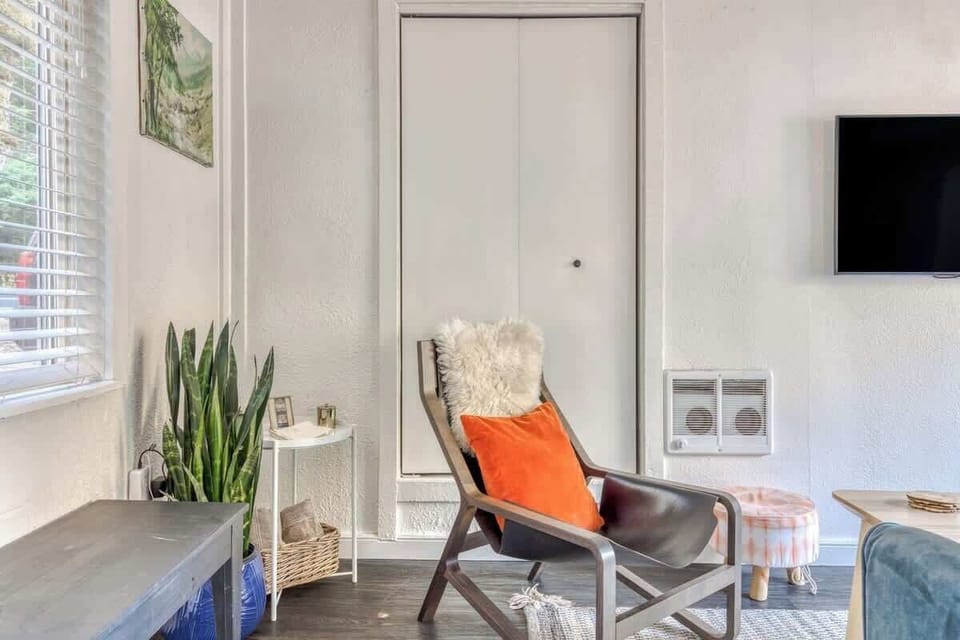 This little corner is giving serious cozy cabin vibes—minimalist but warm. That sheepskin and orange pillow combo on the modern chair adds just the right amount of pop, and the snake plant in the blue pot ties it all together.