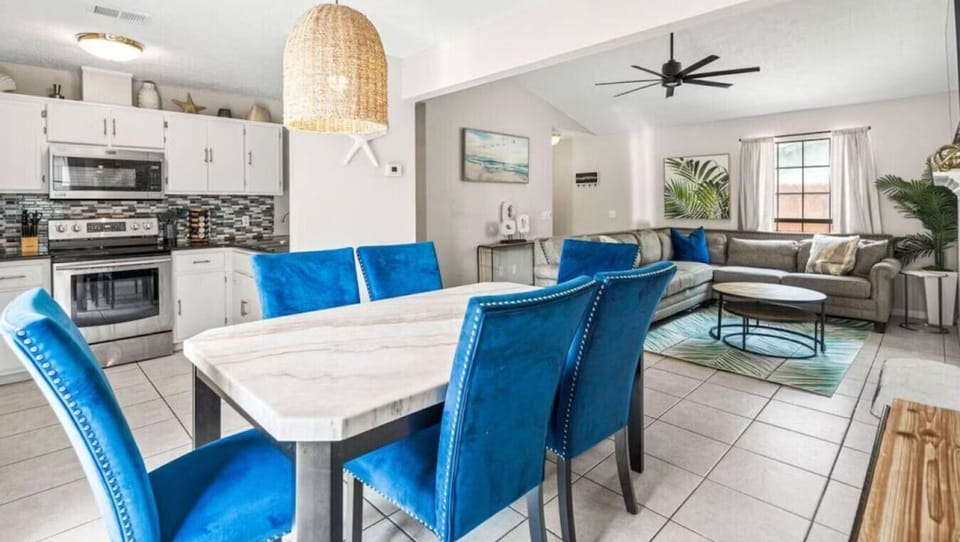 Unwind in your open-plan retreat where vibrant blue chairs invite memorable meals while the spacious living area beckons for cozy evenings together.