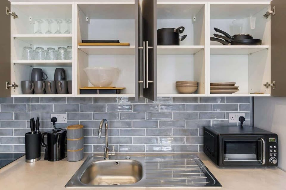 - Modern kitchen with open shelving showing glasses dishes cookware  
- Subway tile backsplash adds style with microwave and storage space  
- Equipped with all essentials for cooking during Airbnb stays  