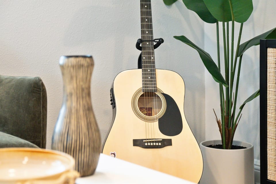 A guitar stands proudly in one corner, its sleek silhouette inviting you to strum a few chords and lose yourself in the magic of music.