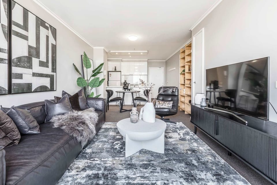 LIVING ROOM: A plush sofa, sweeping city views, and a Smart TV create the perfect setting for slow evenings in. Whether you're lost in a film, caught in a series, or simply savoring the stillness, this space invites you to relax without reason.