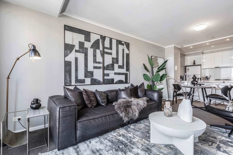 LIVING ROOM: A sleek sanctuary of black-and-white contrasts, where plush seating invites quiet relaxation beside floor-to-ceiling windows capturing the city’s endless rhythm.