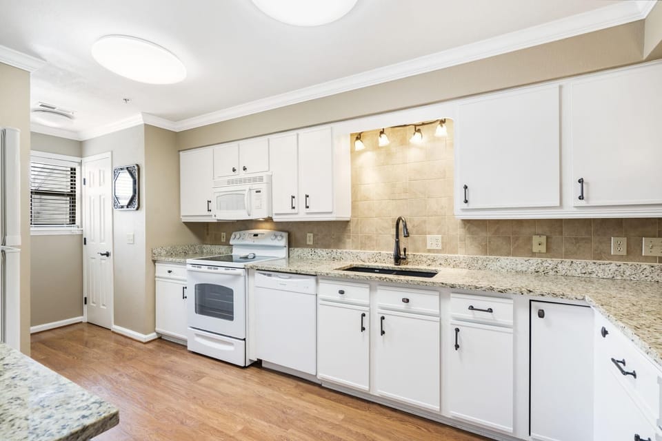 Kitchen with granite countertops, white cabinetry, black faucet, and wood-look flooring under soft ceiling light.