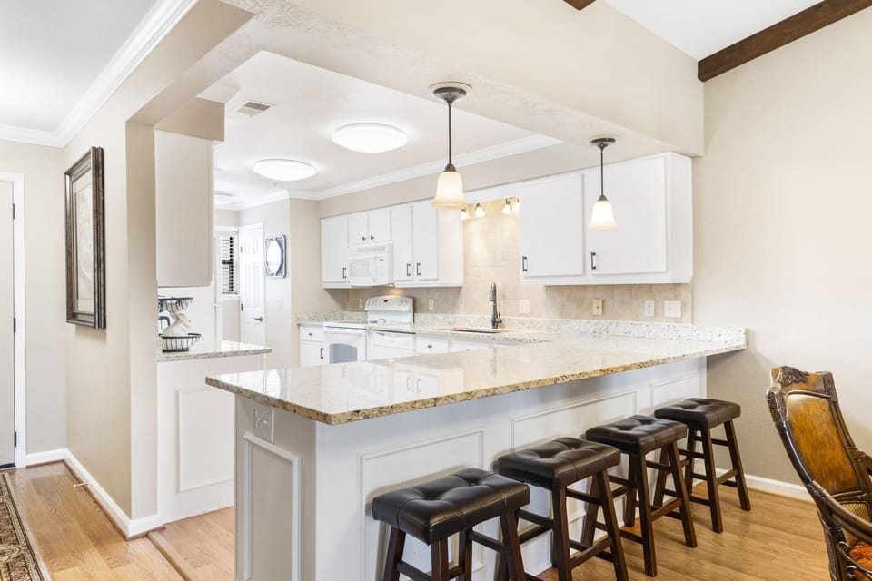 Extended granite countertop breakfast bar with four dark tufted leather stools beneath pendant lights in the kitchen.