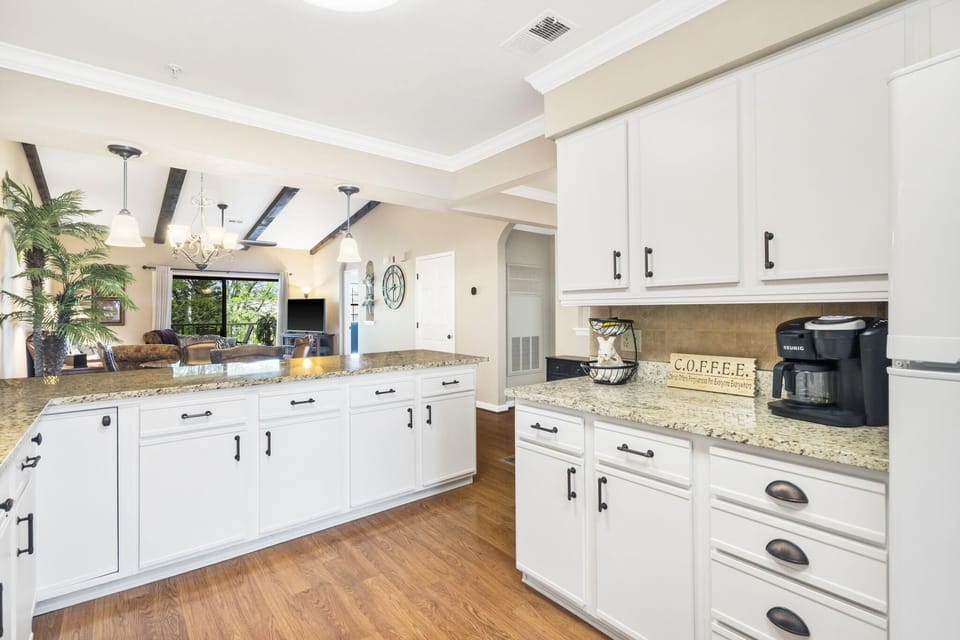 Granite countertops stretch across white cabinetry with black hardware and a black coffee maker on the side counter.