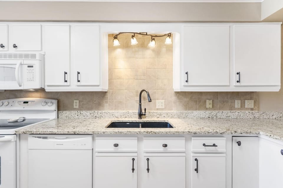 Granite countertops frame a black undermount sink beneath a set of four frosted glass lights in the kitchen.