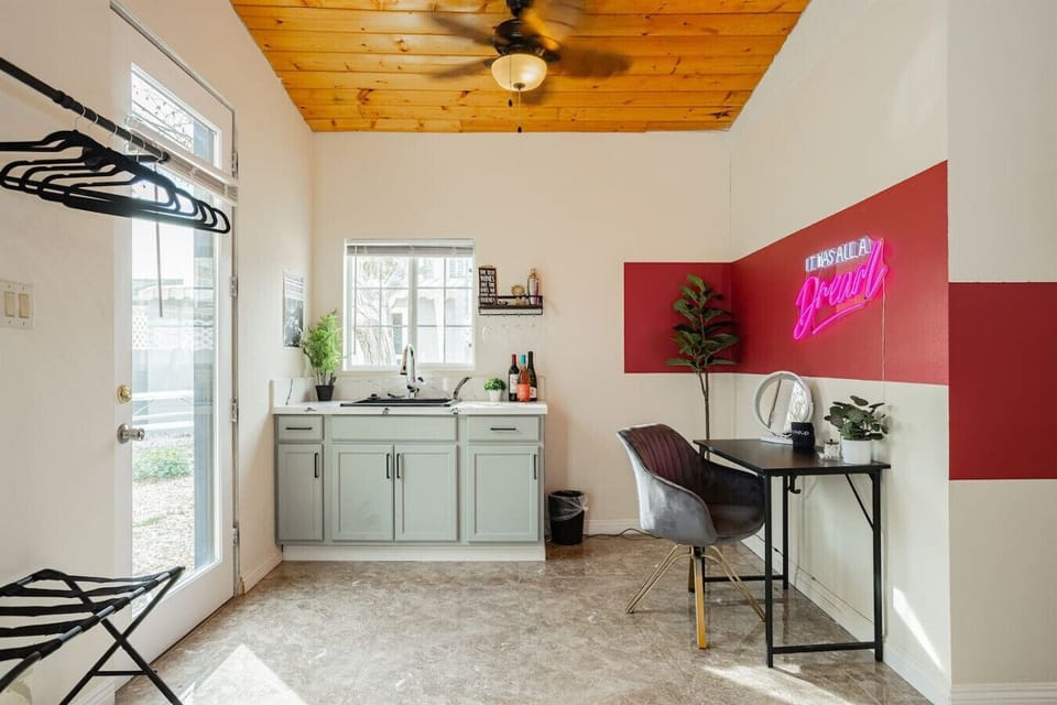 Dedicated Workspace & Wet Bar Nook: Stay connected and productive on your trip with this stylish remote work station featuring a private desk, cushioned velvet chair, pink neon wall sign, luggage rack, and an adjacent wet bar station with built-in sink an
