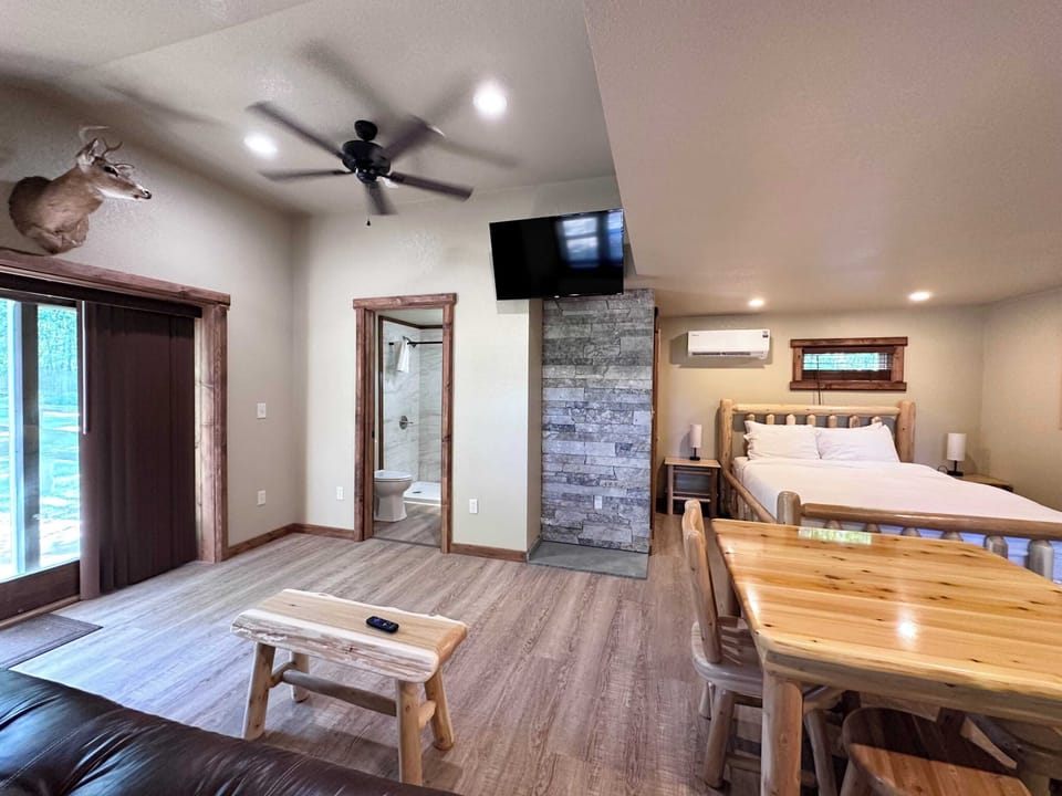 Sitting area with wood coffee table, large tv, ceiling fan, wood framed doorway, sliding glass door and log dining table.