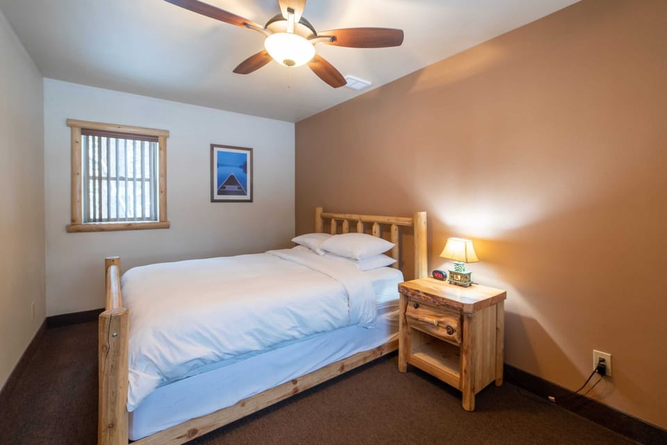Bedroom view with large window, ceiling fan, and log furniture, including a wood queen sized bed, and nightstand.