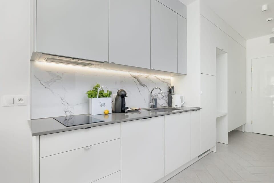 A sleek white kitchen with handleless cabinets and a built-in countertop workspace.