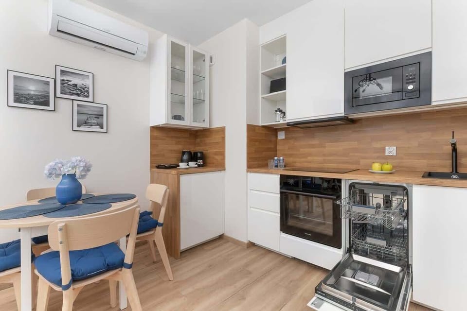 A white and wood-accented kitchen equipped with modern appliances and a dining table.

