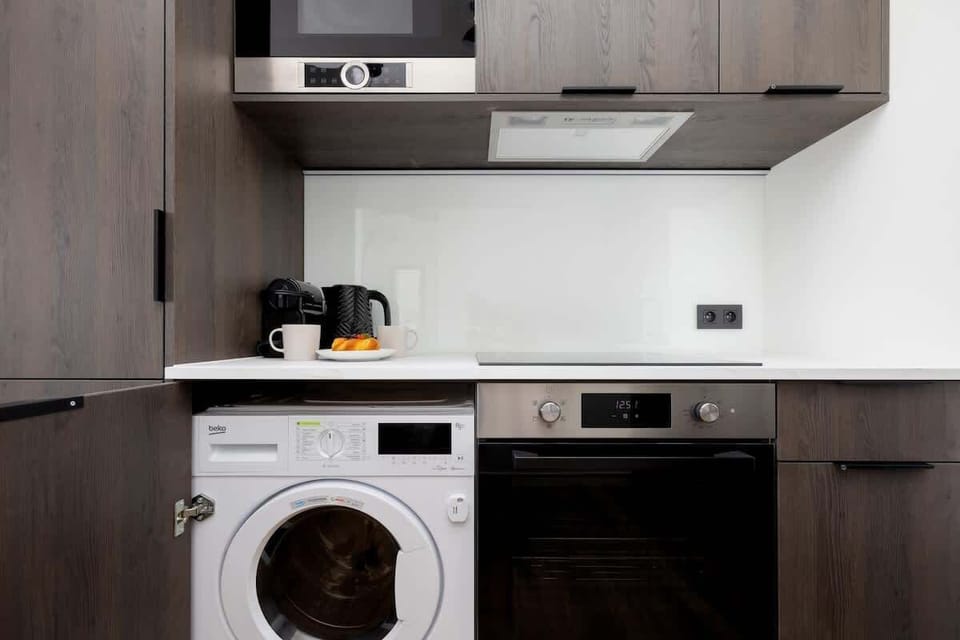 A compact kitchen featuring an oven, stovetop, and washing machine below the counter.


