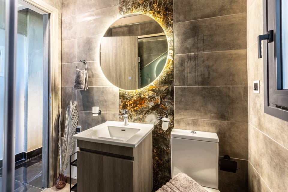 Contemporary Bathroom with Illuminated Mirror and Vanity: Refresh yourself in this stylish bathroom, featuring a modern washbasin, illuminated circular mirror, elegant stone-effect wall tiles, and thoughtfully selected fixtures