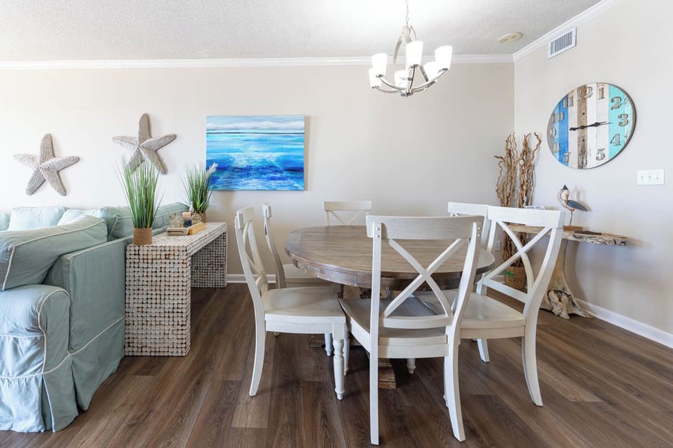 Dine at the round wooden table surrounded by comfortable chairs, with coastal decor enhancing the inviting atmosphere