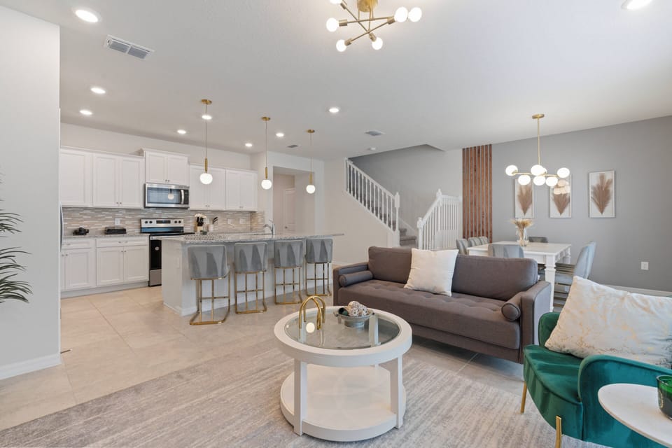 This bright and airy living area boasts a chic gray and white palette, enhanced by stylish pendant lights. The inviting sofa beckons you to relax, and the open layout flows effortlessly into a modern kitchen with sleek cabinetry.