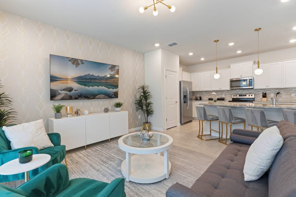 Enjoy a bright living area with a sleek gray sofa and vibrant teal chairs against light walls. The modern kitchen boasts stylish cabinetry and elegant pendant lighting, perfect for casual dining and entertaining.