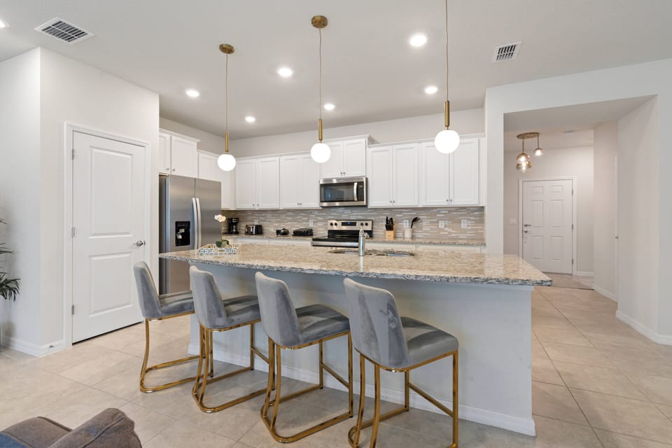 This bright kitchen boasts sleek white cabinets and elegant pendant lighting, enhancing its spacious layout. The island is ideal for casual dining, while the polished countertops inspire your culinary creativity.